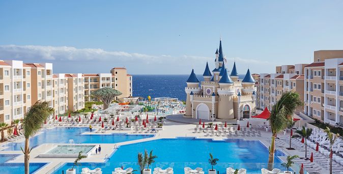 Große Hotelanlage mit mehreren mehrstöckigen Gebäuden, großem Pool, einem märchenhaften Schlossgebäude in der Mitte und Blick auf das Meer im Hintergrund