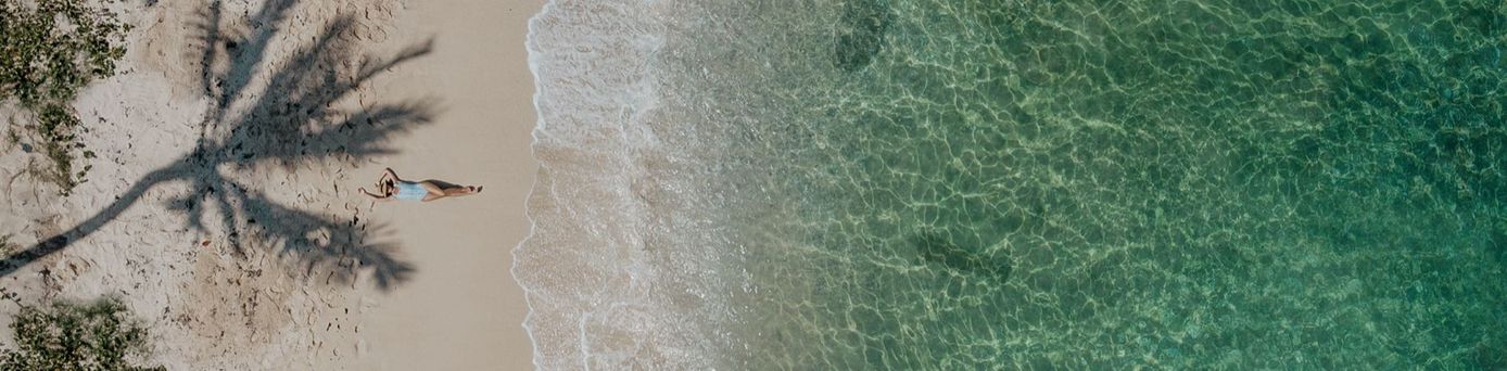 Eine Person liegt auf einem Strand mit Wasser und einer Palmen-Schattenzeichnung im Sand.