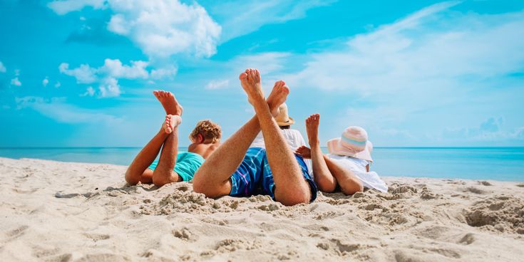Vater und Kinder liegen am Sandstrand mit Blick auf das Meer unter blauem Himmel und genießen einen Strandurlaub am Wasser