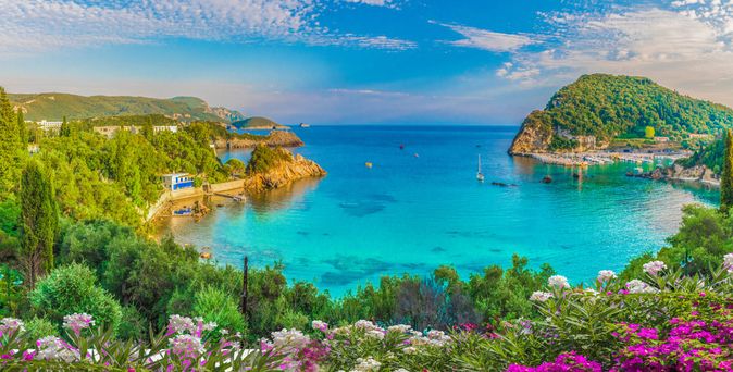 Bucht von Paleokastritsa in Griechenland mit türkisblauem Wasser, grünen Hügeln und bunten Blumen im Vordergrund