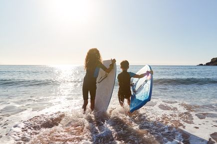 Zwei Kinder mit Surfboards laufen ins Meer, bereit zum Wellenreiten im Sonnenlicht
