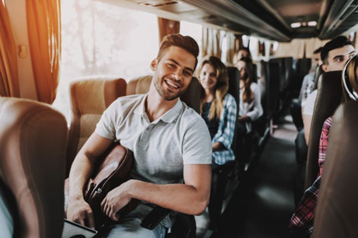 Mann sitzt in einem Bus und hält eine Tasche auf dem Schoß, weitere Passagiere sitzen hinter ihm