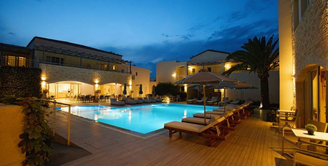 Beleuchteter Außenpool mit Liegen und Sonnenschirmen vor einem mehrstöckigen Hotelgebäude bei Abenddämmerung