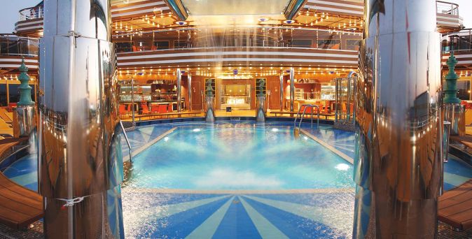 Der Lido Stella del Sud Pool auf der Costa Diadema mit Wasserfontäne, Liegebereichen und abendlicher Beleuchtung in elegantem Schiffsumfeld