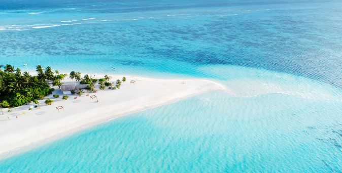 Luftaufnahme eines weißen Sandstrandes auf den Malediven mit tropischer Vegetation, Palmen und türkisblauer Lagune, die sich entlang einer schmalen Inselzunge erstreckt