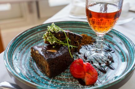 Stücke von Bolo de Mel, traditionellem Honigkuchen aus Madeira, auf einem dekorativen Teller mit Erdbeere und einem Glas Likör