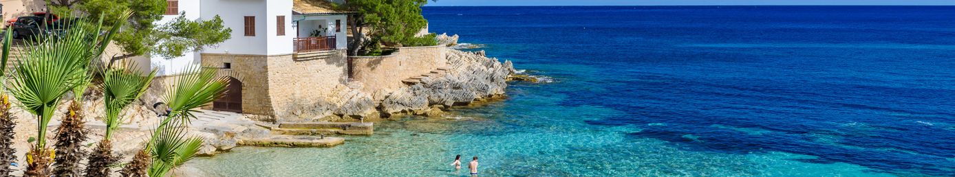 Kleine Badebucht Cala Ratjada auf Mallorca mit klarem Wasser, Felsen und grünen Pinien am Strand