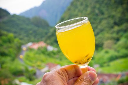 Glas Poncha, traditionelles Getränk aus Madeira mit Maracuja, vor grüner Berglandschaft und einem Tal im Hintergrund