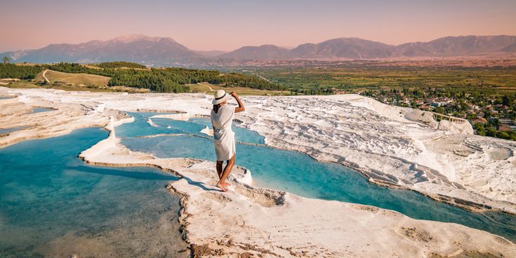 Weiße Kalkterrassen von Pamukkale in der Türkei mit türkisfarbenen Thermalbecken und Blick auf die Berge im Hintergrund