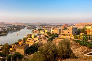 Blick auf den Nil und die Stadt Assuan mit Gebäuden und Vegetation am Flussufer bei klarem Himmel