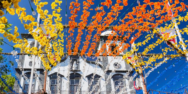 Kirche auf Madeira mit bunten Blumenketten in Gelb und Orange, die über dem Platz gespannt sind
