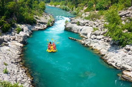 Gruppe beim Rafting auf einem türkisblauen Fluss, umgeben von Felsen und dichtem Grün