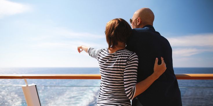 Zwei Personen stehen an der Reling eines Kreuzfahrtschiffs, blicken auf das Meer und eine Person zeigt auf den Horizont