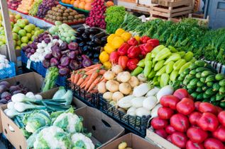 Bunter Marktstand mit frischem Gemüse wie Paprika, Tomaten, Karotten, Zwiebeln und Gurken