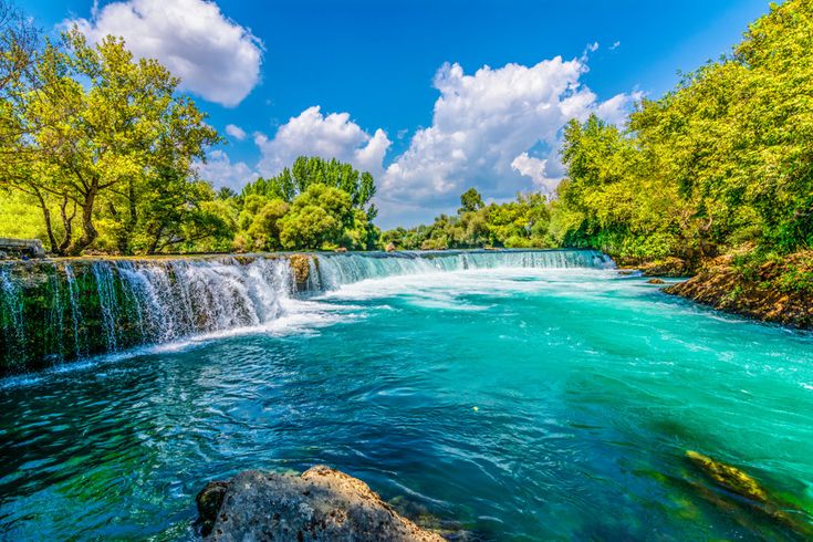 Manavgat-Wasserfall in der Türkei mit türkisblauem Wasser, grünen Bäumen und blauem Himmel mit weißen Wolken