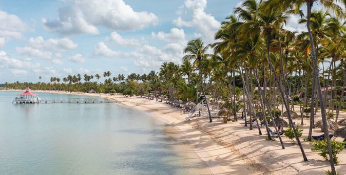 Strand mit Palmen und Steg am Bahia Principe Grand La Romana Resort unter blauem Himmel mit Wolken