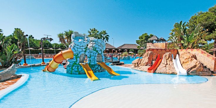 Flacher Kinder-Wasserpark mit bunten Rutschen, künstlichen Felsen, Wasserspielen und tropischen Pflanzen in einer weitläufigen Poollandschaft des Protur Badía Park Aparthotels