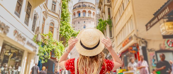 Person mit Strohhut steht in einer belebten Straße und blickt auf den historischen Galataturm in Istanbul