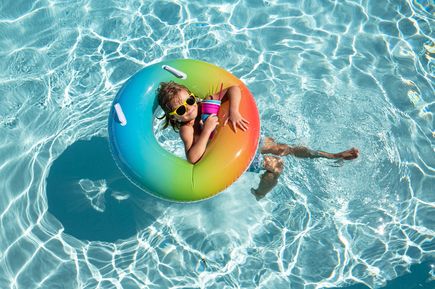 Kind entspannt im bunten Schwimmreifen im klaren Poolwasser und genießt den Sommerurlaub