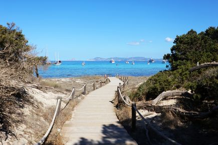 Holzsteg führt durch Dünen zum türkisblauen Meer am Strand Cavall d'en Borràs auf Formentera, mit Segelbooten im Hintergrund