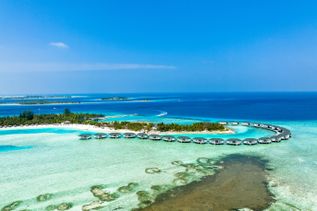 Luftaufnahme eines halbkreisförmigen Stegs mit Bungalows über türkisfarbenem Wasser und einer Insel mit Palmen im Hintergrund