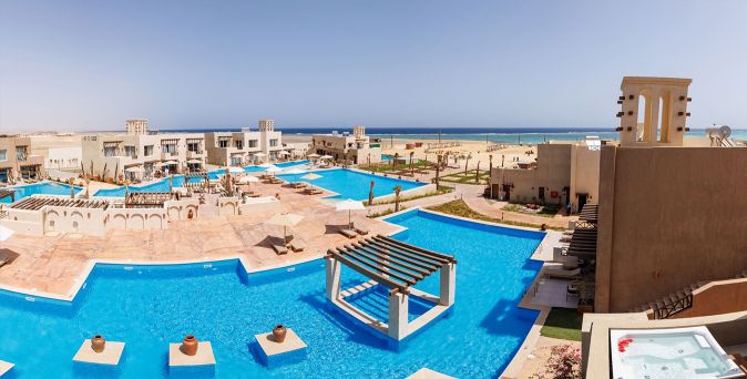 Blick auf das True Beach Village in Ägypten mit Poollandschaft und niedrigen Bungalows mit dem Meer im Hintergrund.