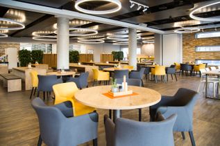 Kantine in Gebäude 3 von schauinsland-reisen mit runden Tischen, gepolsterten Stühlen in Gelb- und Grautönen, Holzoberflächen, Pflanzen und moderner Beleuchtung