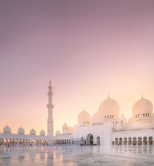 Weitläufiger Innenhof der Scheich-Zayid-Moschee in Abu Dhabi bei Sonnenuntergang mit weißen Kuppeln und hohen Minaretten.