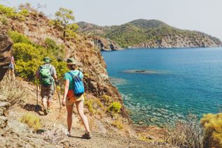 Gruppe von Wandernden auf einem Küstenpfad mit Blick auf das türkisblaue Meer und bewaldete Hügel