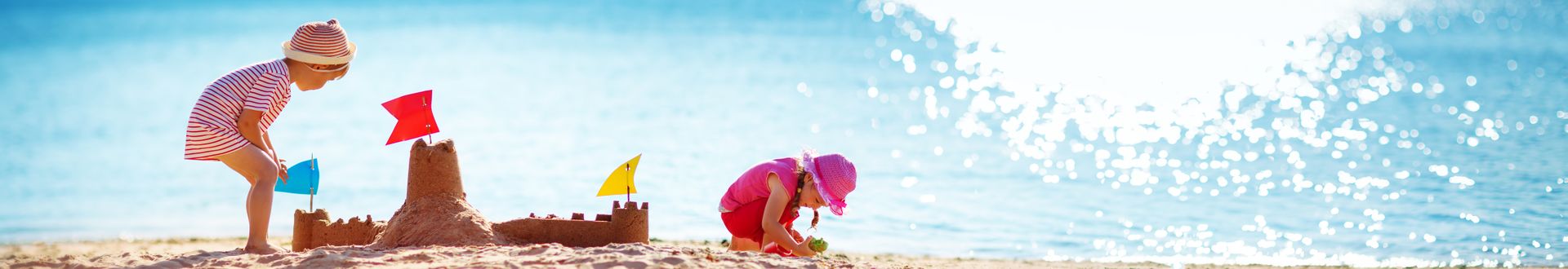 Zwei Kinder bauen eine Sandburg mit bunten Fahnen am Strand direkt am Meer