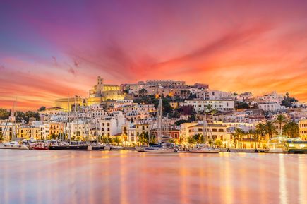 Beleuchtete Altstadt von Ibiza mit Hafen und Segelbooten bei farbenprächtigem Sonnenuntergang
