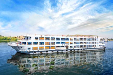 Flusskreuzfahrtschiff MS Nile Serenity mit mehreren Decks und großen Fenstern auf dem Nil unter bewölktem Himmel