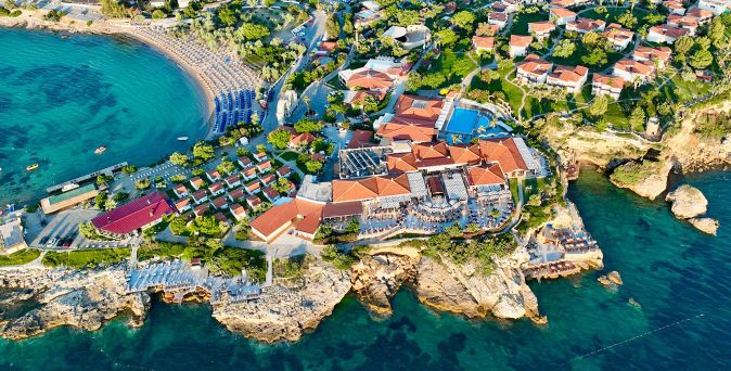 Luftaufnahme des Club Resort Atlantis an einer malerischen Badebucht mit weitläufiger Hotelanlage, Poolbereich, Strandabschnitt und türkisblauem Meer entlang der felsigen Küste.