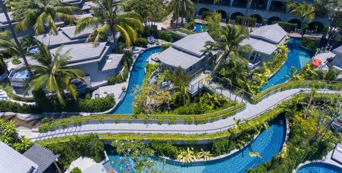 Luftaufnahme des Meliá Koh Samui Resorts mit mehreren Bungalows, umgeben von Palmen und einem geschwungenen Lagunenpool mit Brücken und Wegen