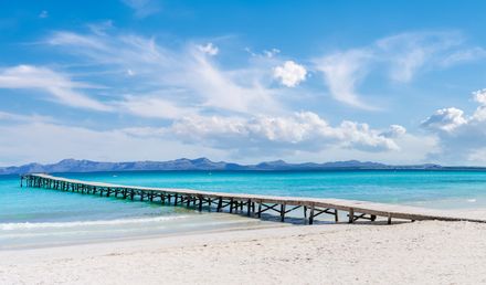 Heller Sandstrand Playa de Muro bei Can Picafort auf Mallorca mit Holzsteg ins türkisfarbene Meer und Bergen im Hintergrund