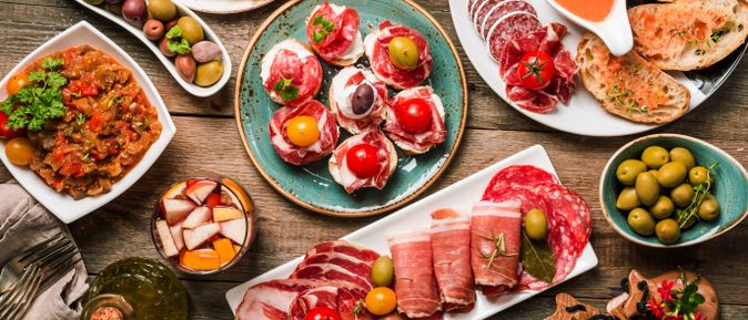 Auswahl spanischer Tapas auf Holztisch, darunter Oliven, Aufschnitt, Brot mit Tomate, Gemüsegericht und Sangria
