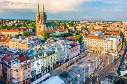 Panoramablick auf die Altstadt von Zagreb in Kroatien mit dem Ban-Jelačić-Platz, historischen Gebäuden, Straßenbahnen und der markanten Kathedrale von Zagreb im Abendlicht