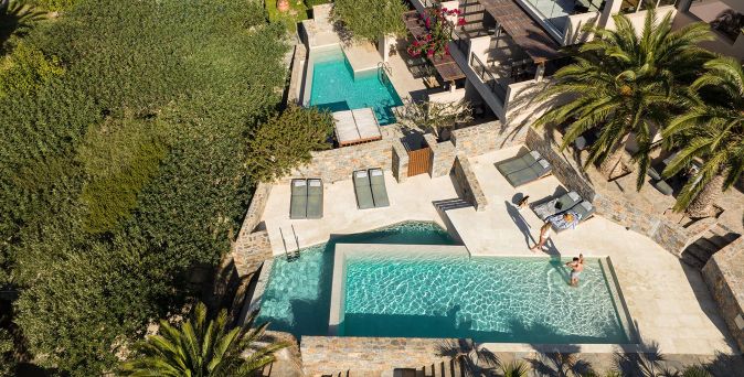 Luftaufnahme des Paralos Irina Mare auf Kreta mit mehreren Naturstein-Pools, Sonnenterrassen und Palmen in ruhiger Umgebung