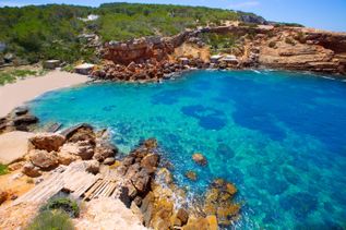 Kleine Bucht bei Punta de sa Galera nahe San Antonio auf Ibiza mit klarem türkisblauem Wasser, Felsen und vereinzelten Fischerhütten