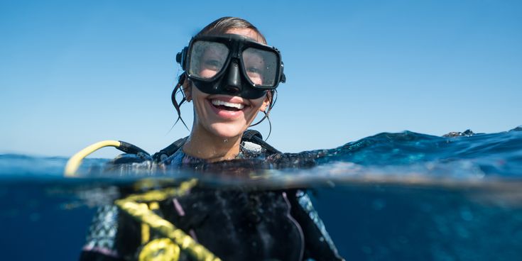 Taucherin mit Tauchmaske und Atemregler im Wasser, halb unter Wasser fotografiert