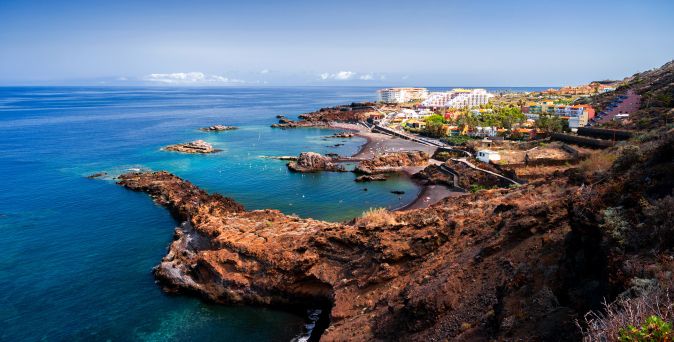 Panorama der Küste von La Palma mit felsigen Ufern, klarem Wasser und einer Ansiedlung im Hintergrund.