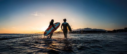 Zwei Surfer mit Boards laufen bei Sonnenuntergang ins Meer