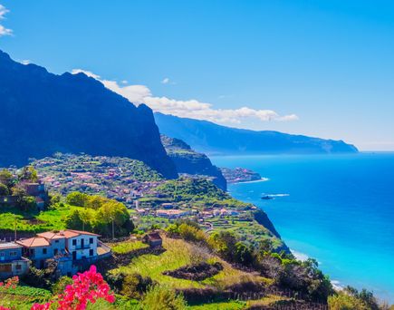 Berglandschaft mit Häusern und grünen Terrassen am Meer auf Madeira unter blauem Himmel