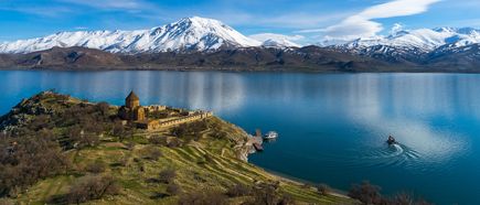 Blick über den türkischen Vansee auf eine kleine Insel mit historischer Kirche, dahinter schneebedeckte Berge und ruhiges, blaues Wasser