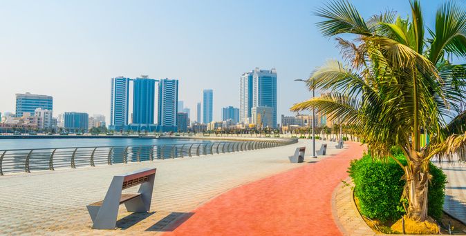 Promenade mit Bänken und Palmen am Wasser, im Hintergrund moderne Hochhäuser in Ajman
