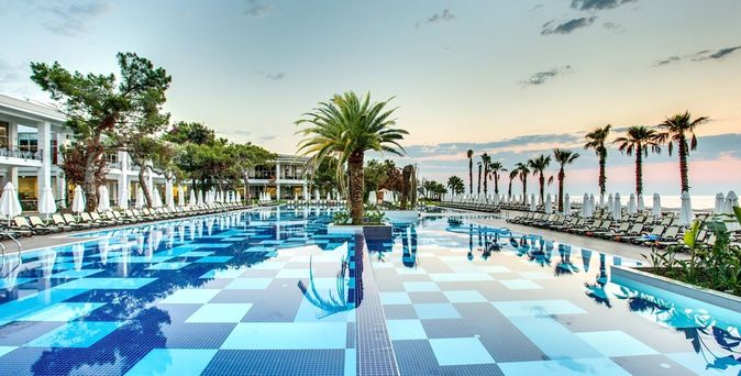 Pool im Sherwood Exclusive Kemer Resort in der Türkei, umgeben von Liegestühlen und Palmen bei Sonnenuntergang