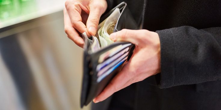 Eine Person öffnet eine schwarze Geldbörse mit Bankkarten und Bargeldscheinen