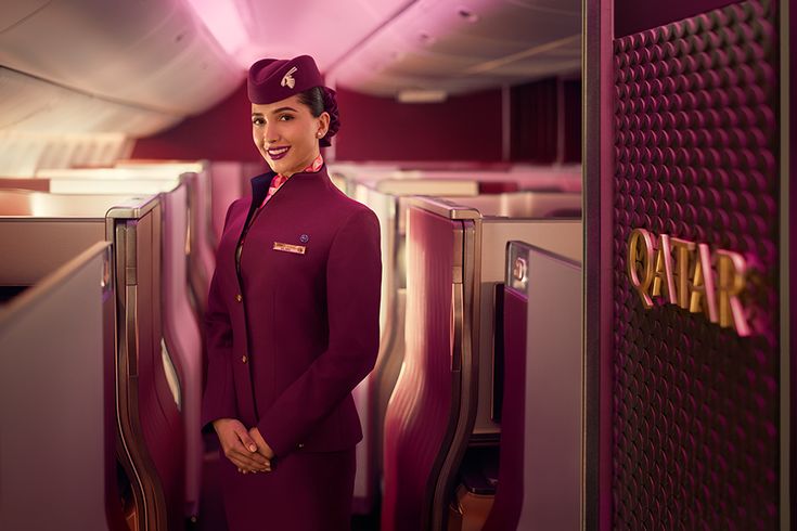 Flugbegleiterin von Qatar Airways steht in der Business Class eines Flugzeugs zwischen modernen Sitzreihen
