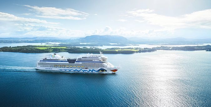 AIDA Kreuzfahrtschiff fährt auf ruhigem Meer vor einer Inselkulisse 