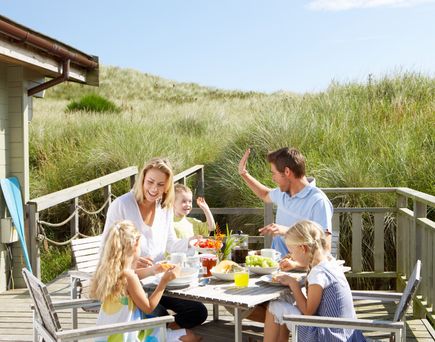 Familie frühstückt gemeinsam auf der Terrasse eines Ferienhauses in den Dünen und genießt entspannten Urlaub in naturnaher Umgebung